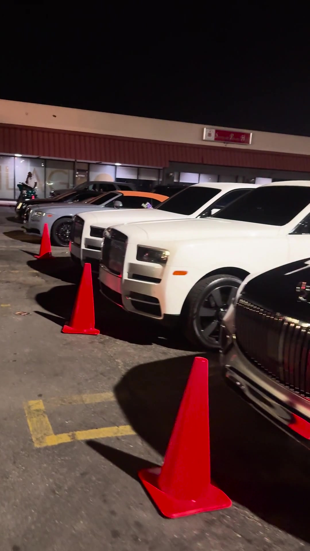 Luxury vehicles beside orange valet cones at night